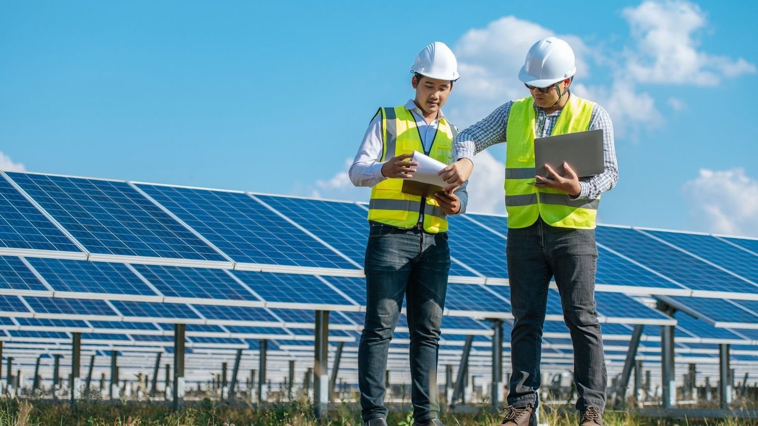 Dos técnicos de prevención revisando documentación en tableta frente a los seguidores de un parque fotovoltaico